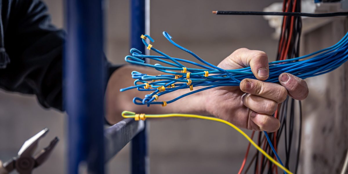 A construction electrician cuts a voltage cable during a repair, close up.